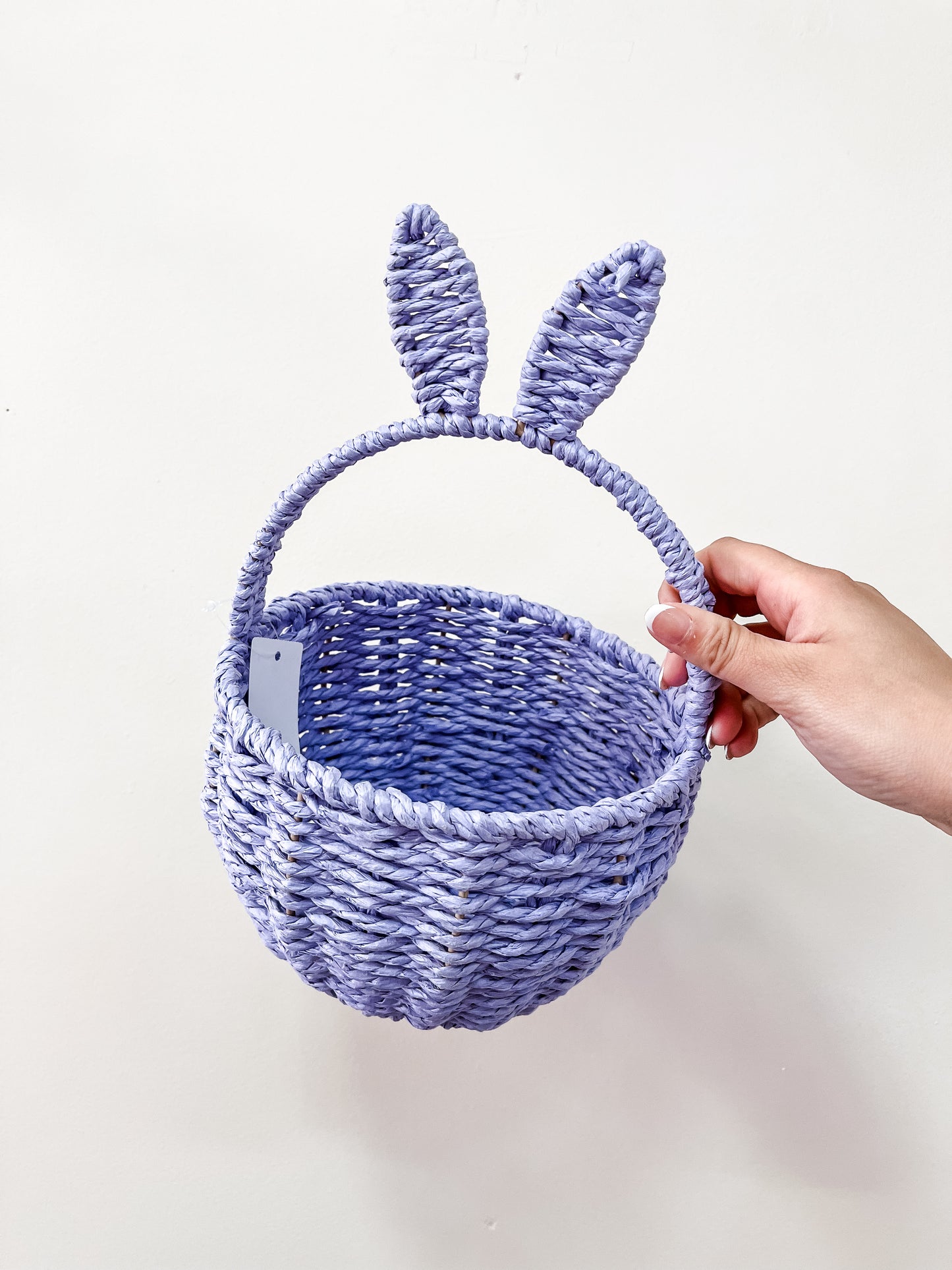 A hand holds the Capzone Pastel Bunny Ear Basket, a light purple woven basket with two upright bunny ear handles, against a plain white background.