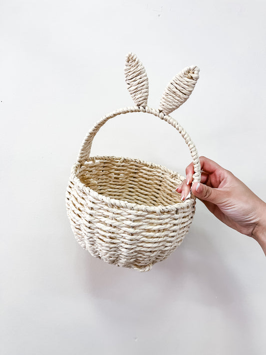 A hand holds the Capzone Pastel Bunny Ear Basket, featuring a woven straw design with bunny ear-shaped handles, against a plain white background.