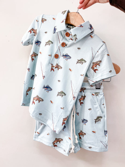 The Fishing Day Lounge Set by Tiny Tot Bundles features a light blue short-sleeve shirt and matching shorts with fish, turtle, and fishing rod designs, displayed on a wooden hanger against a white background.