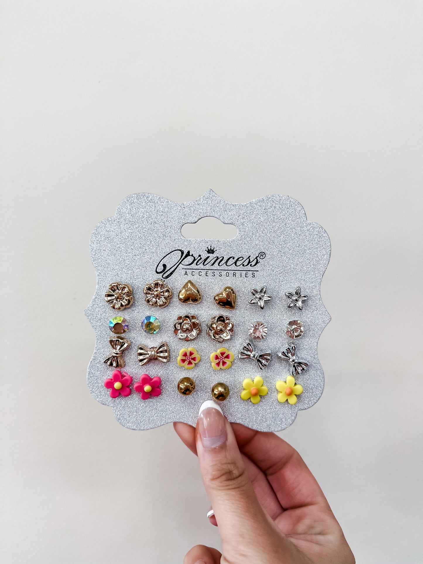 A hand holds the funteze Princess Earing Set—18 colorful gold, pink, and yellow studs on a glittery card, with flowers, hearts, bows, and crystal designs.