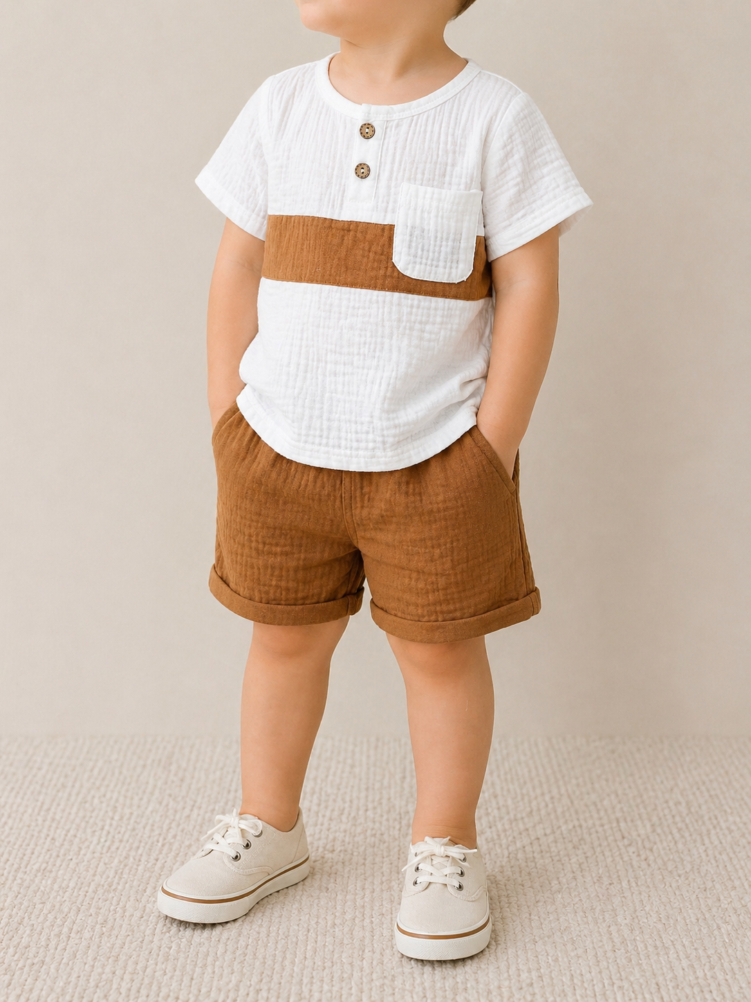 A young child wears the Tiny Tot Bundles Linen Classic Set, featuring a white short-sleeve shirt with a brown stripe and pocket, matching brown shorts, and beige lace-up shoes, standing against a neutral backdrop.