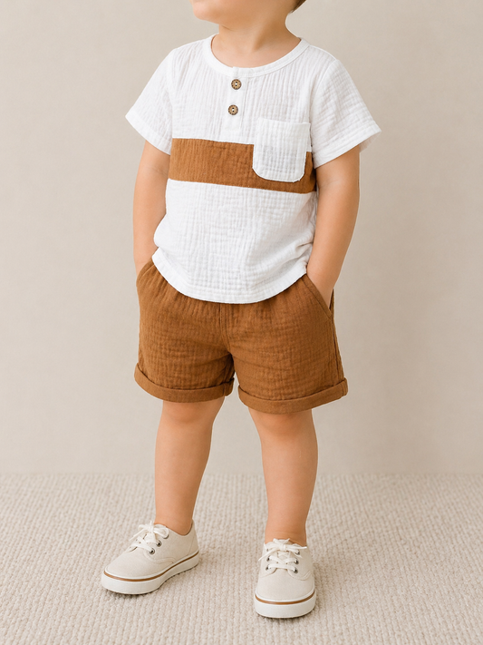 A young child wears the Tiny Tot Bundles Linen Classic Set, featuring a white short-sleeve shirt with a brown stripe and pocket, matching brown shorts, and beige lace-up shoes, standing against a neutral backdrop.