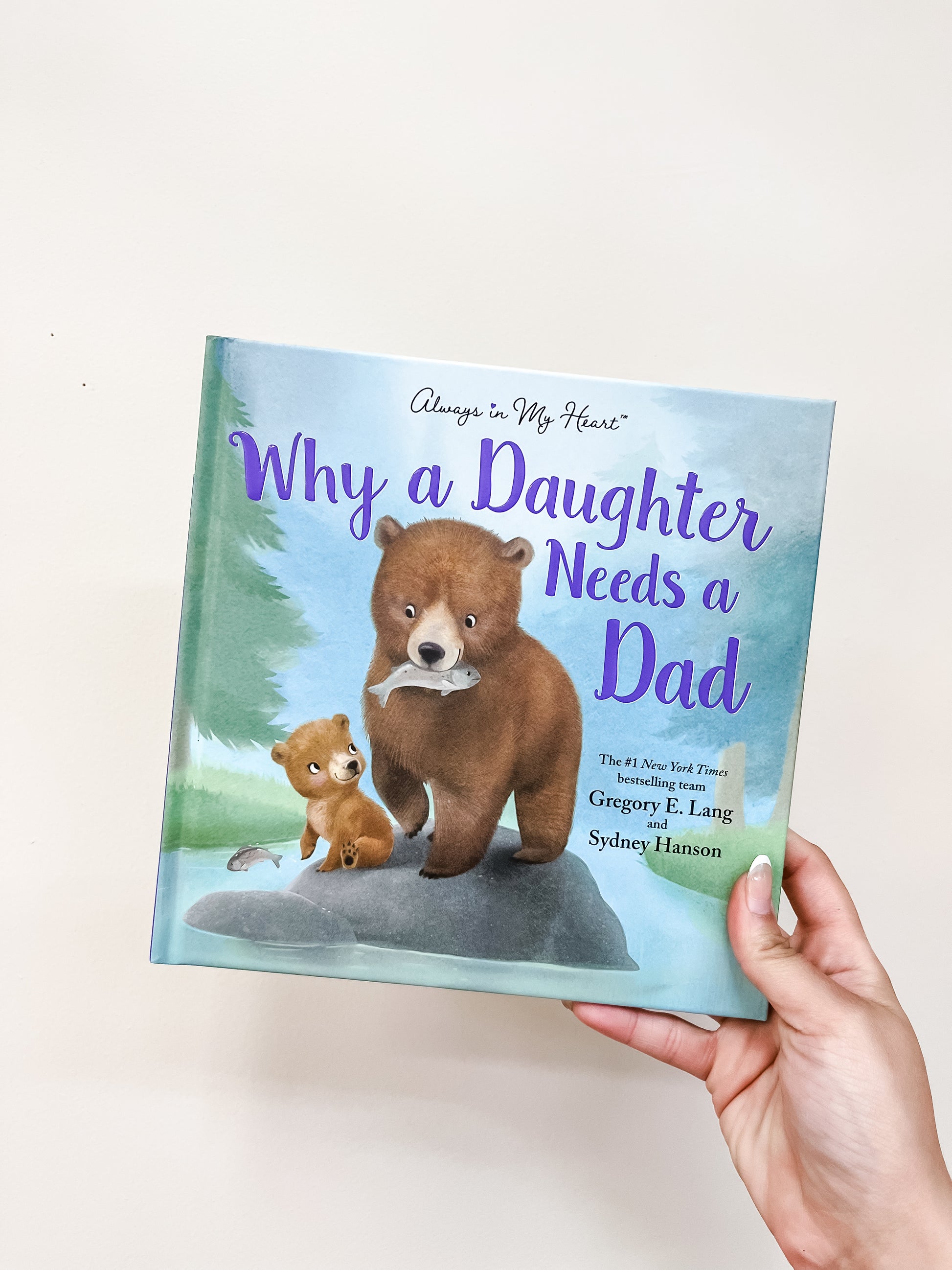 A hand holds the sour brand "Why A Daughter Needs A Dad Book," featuring an adult bear and a cub on the cover.
