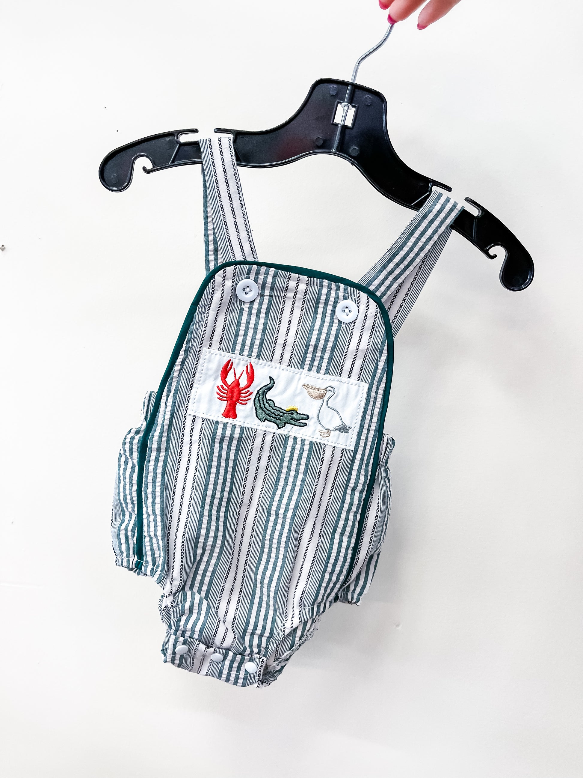 The Seaside Stripe Romper by Tiny Tot Bundles features green and white vertical stripes with an embroidered patch of a red lobster, green alligator, and white pelican, displayed on a black hanger.