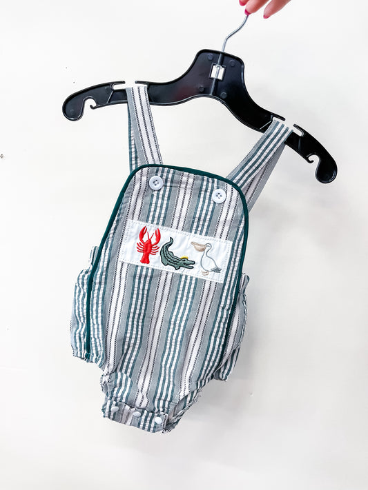 The Seaside Stripe Romper by Tiny Tot Bundles features green and white vertical stripes with an embroidered patch of a red lobster, green alligator, and white pelican, displayed on a black hanger.