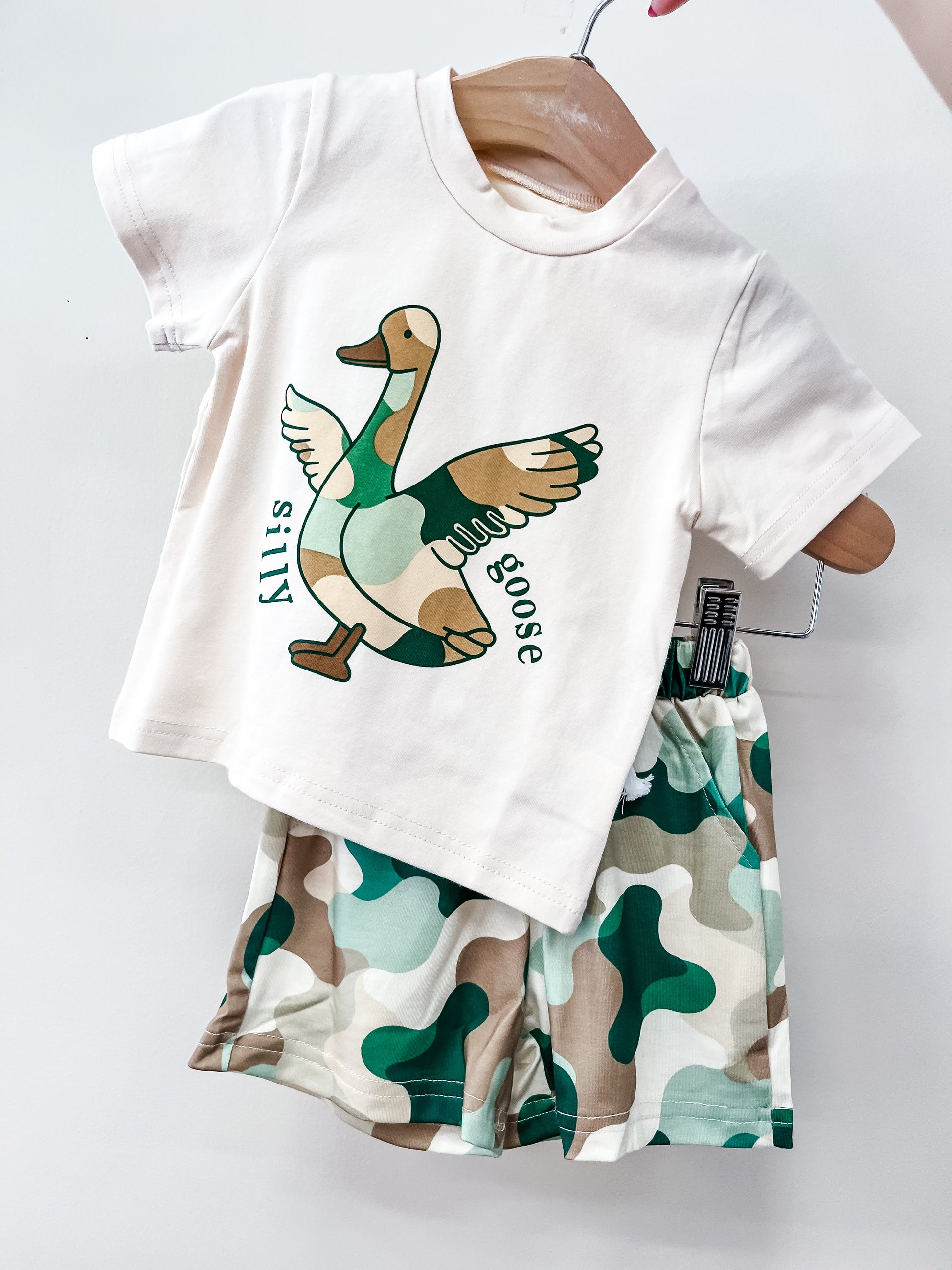 The Tiny Tot Bundles Waddlin’ West Short Set features a white t-shirt with a silly goose graphic, paired with green, beige, and white camo shorts—perfect for playful kids.