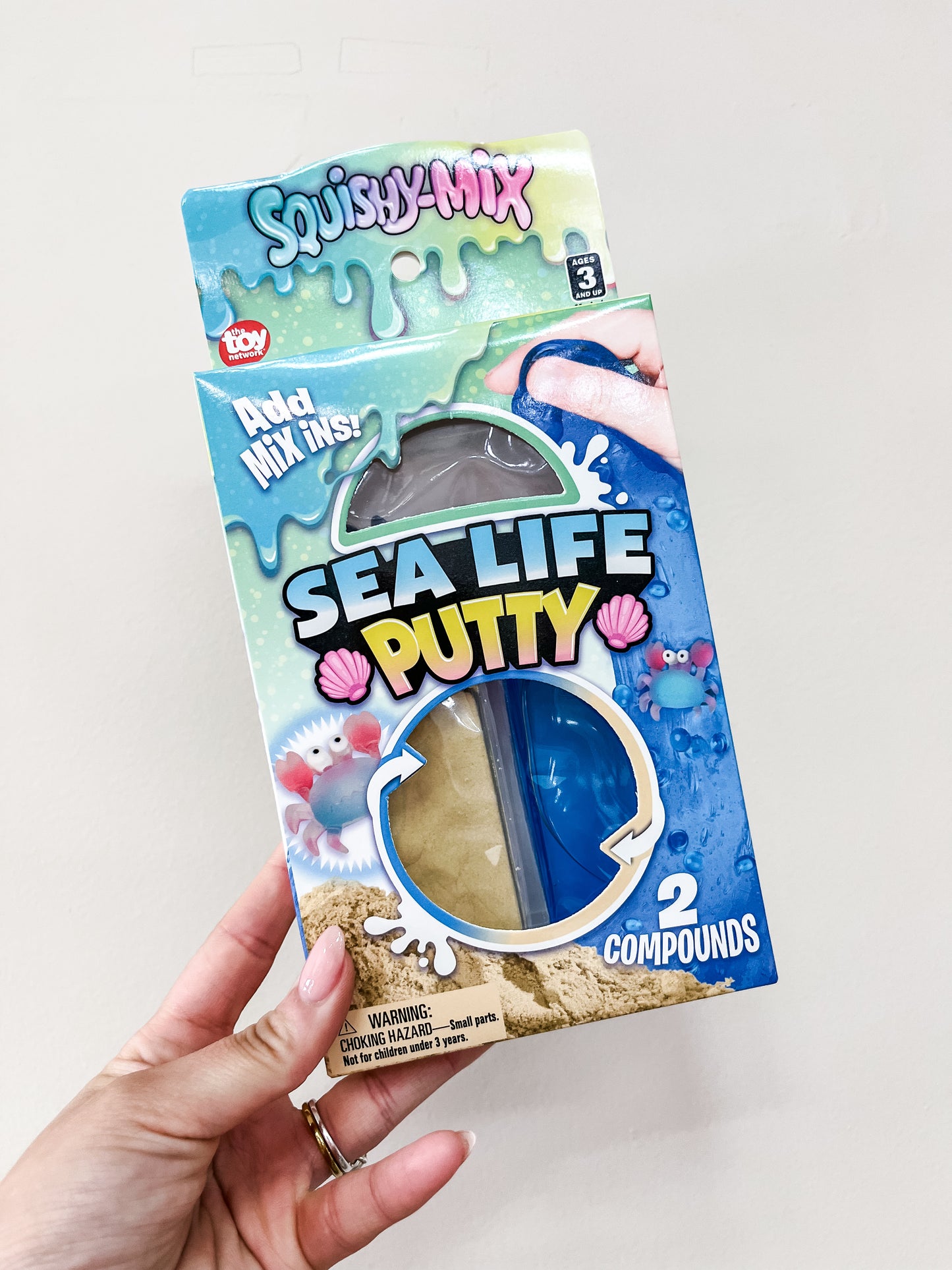A hand holds a box of Ocean Mix-In Putty Set from The Toy Network, featuring two colored putty compounds. The blue packaging shows sea creatures and seashells.