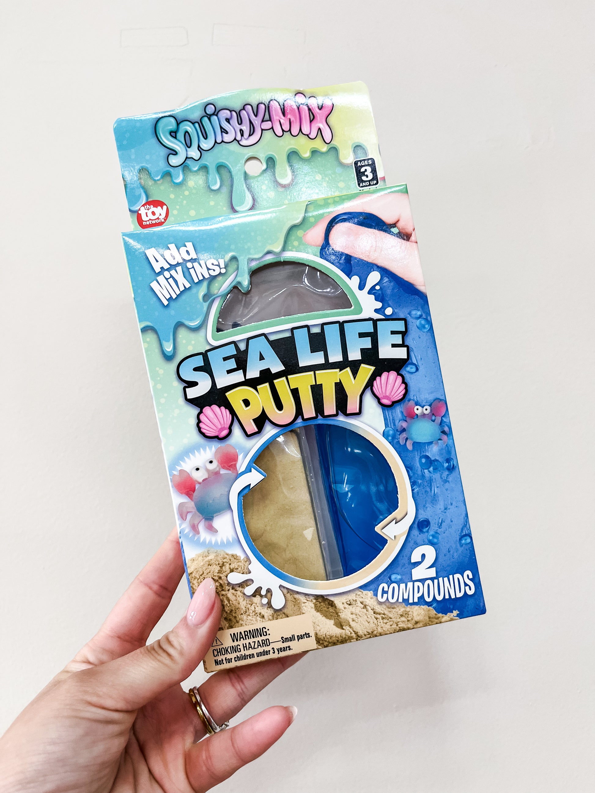 A hand holds a box of Ocean Mix-In Putty Set from The Toy Network, featuring two colored putty compounds. The blue packaging shows sea creatures and seashells.