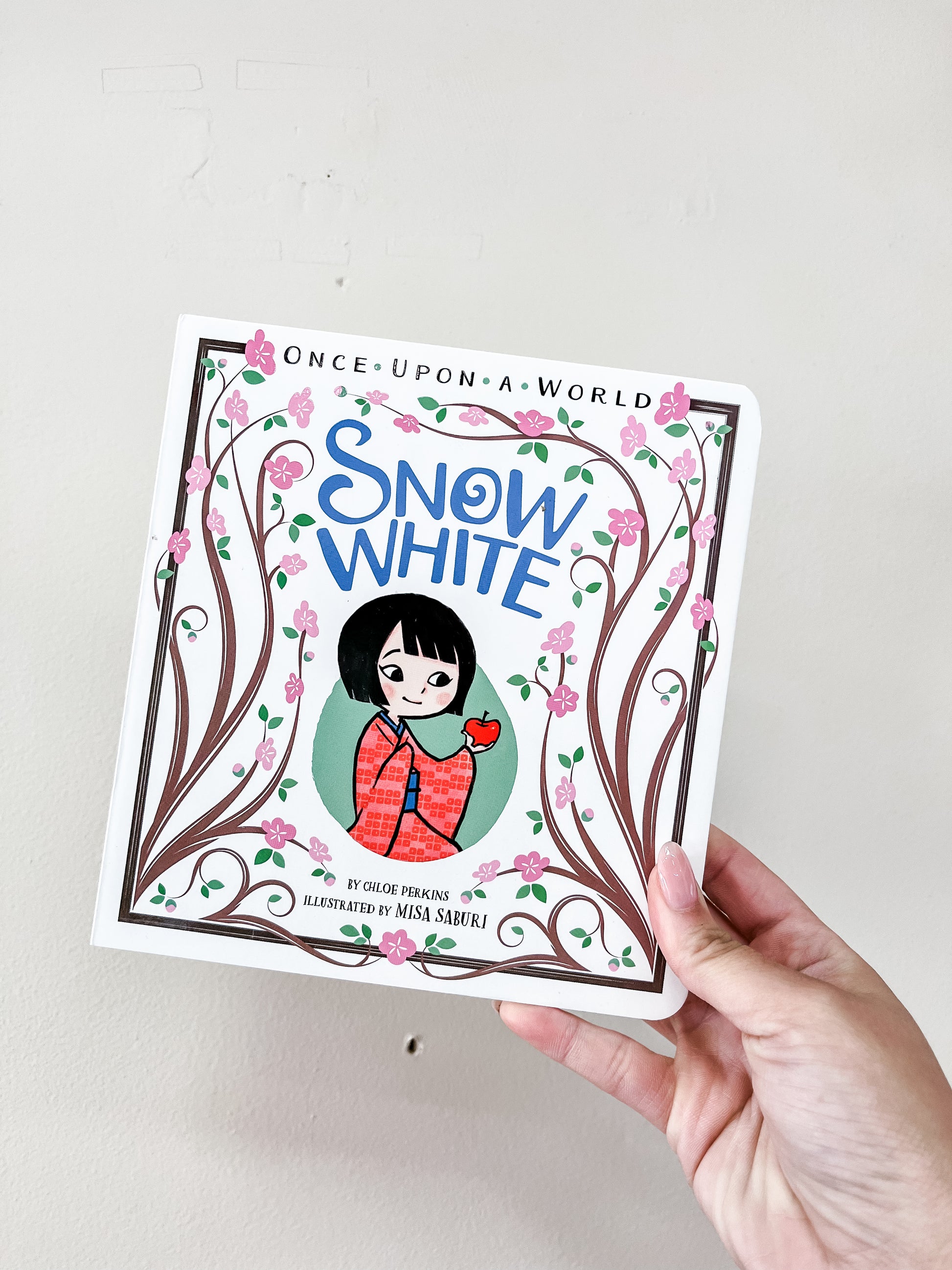 A hand holds the Snow White Book by Simon & Schuster, featuring an illustrated girl in red with an apple on the cover, framed by decorative vines and pink flowers.