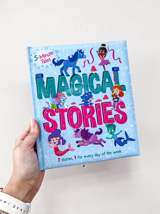 A hand holds Simon & Schuster’s 5 Minute Tales: Magical Stories Book, featuring a blue, starry cover with colorful illustrations of fairies, unicorns, and magical creatures.