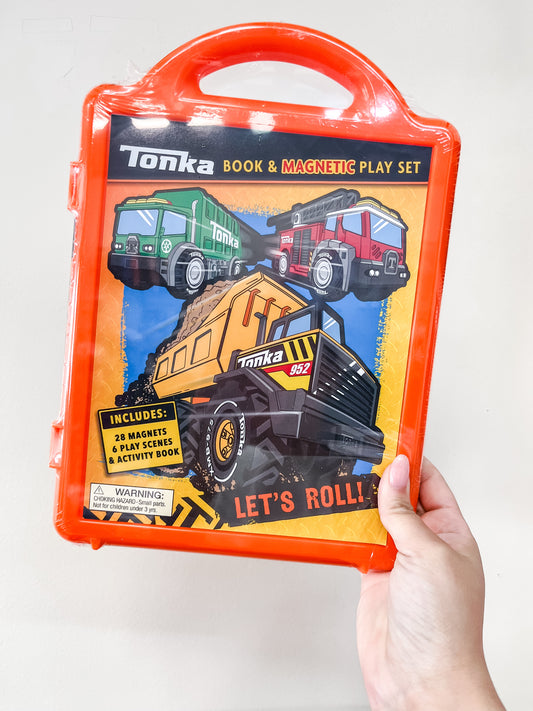 A hand holds the Simon & Schuster Tonka: Magnetic Play Set: Let's Roll Book in an orange case, featuring construction truck illustrations and the text "Let's Roll!" The set includes magnets, play scenes, and an activity book.