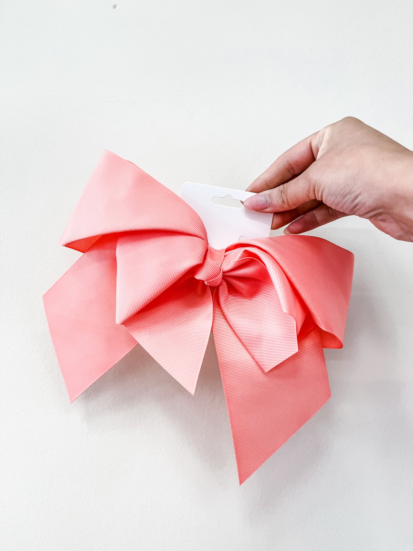 A hand holds the funteze Classic Statement Bow—a large pink decorative bow on a white card—against a plain white background.