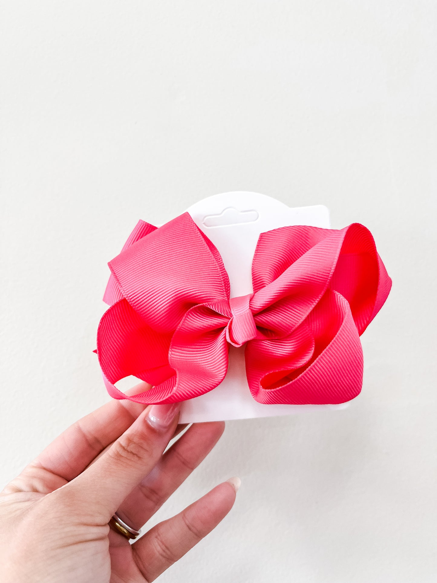 A hand holds a white card displaying the funteze Classic Boutique Bow in bright pink, set against a plain white background.
