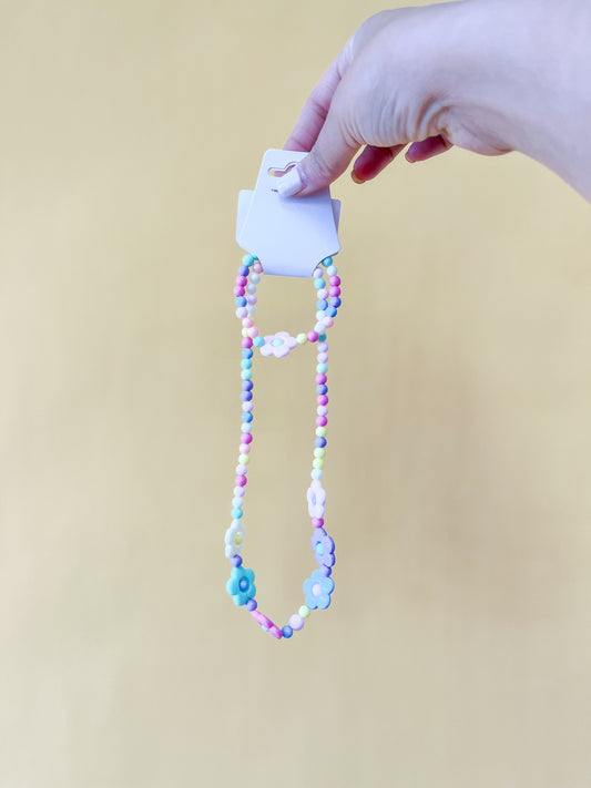 A hand holds a card displaying the Tiny Tot Bundles Daisy Bracelet Set, featuring colorful pastel and flower-shaped beads, against a plain yellow background.