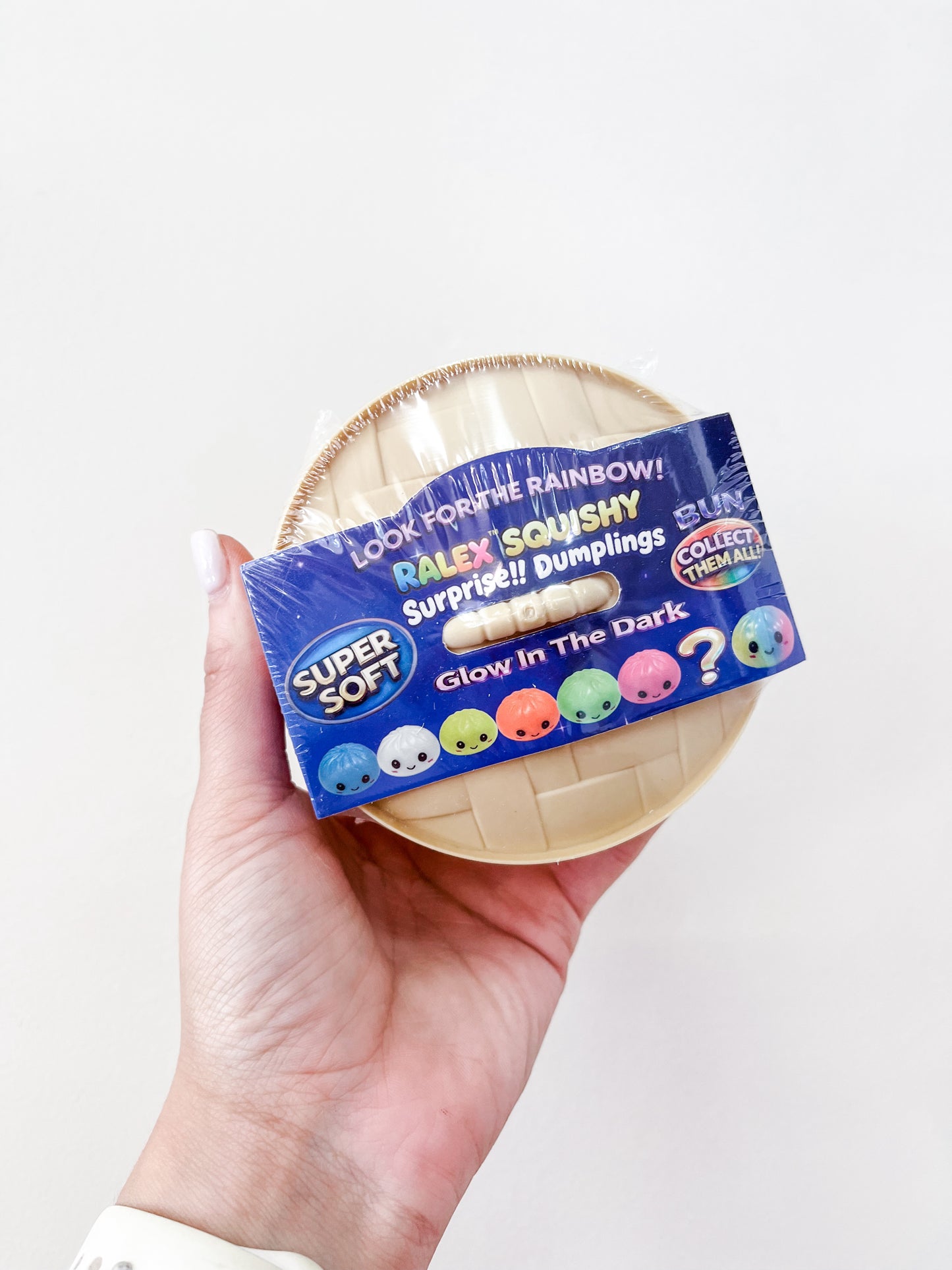 A hand holds a round blue package labeled Prime Opticals Glow in the Dark Dumpling, featuring Super Soft text and colorful dumpling characters.