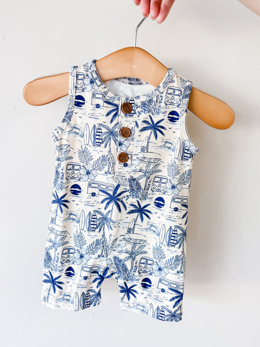 The Surfside Florida Tank Romper by Tiny Tot Bundles is a sleeveless baby romper with a blue tropical print of palm trees, surfboards, and camper vans, shown on a wooden hanger held against a plain white background.