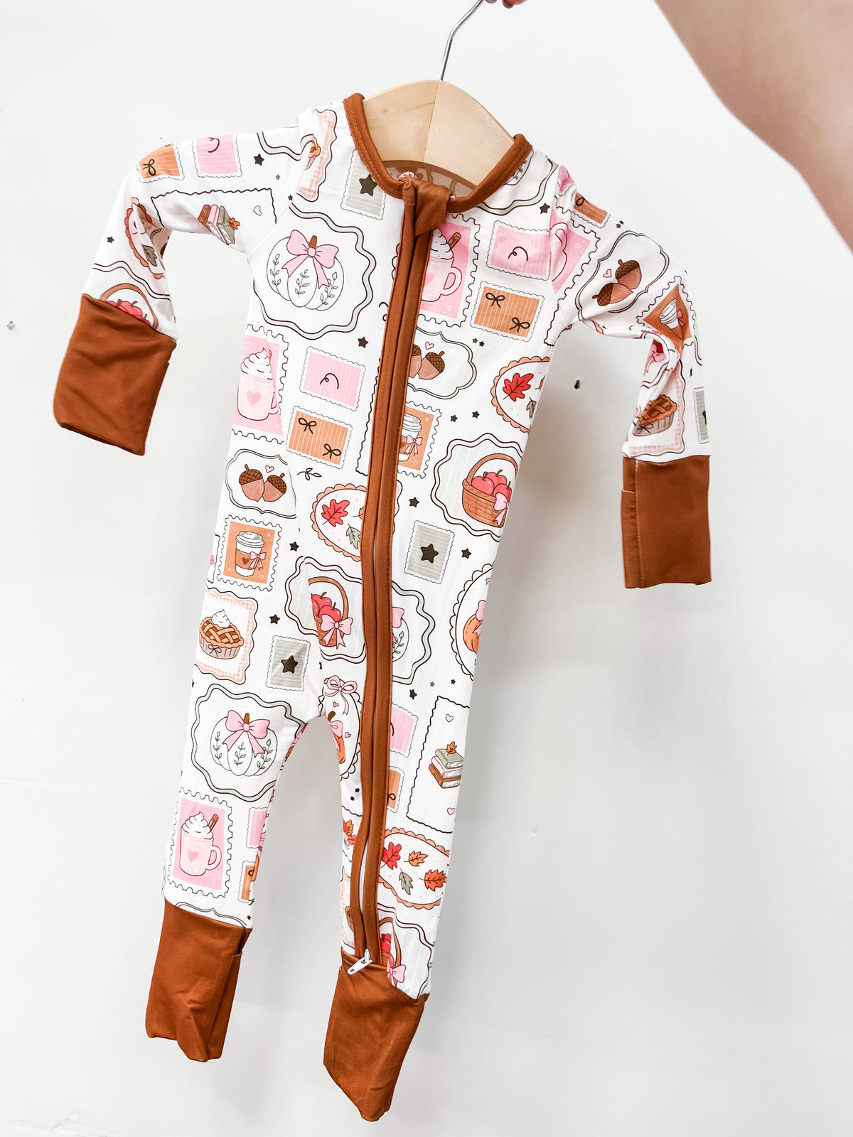 Tiny Tot Bundles Fall Favorites Zippy, a long-sleeved baby romper with a front zipper, a white pattern of fall-themed postage stamps featuring pies, mugs, and acorns, and solid brown cuffs.