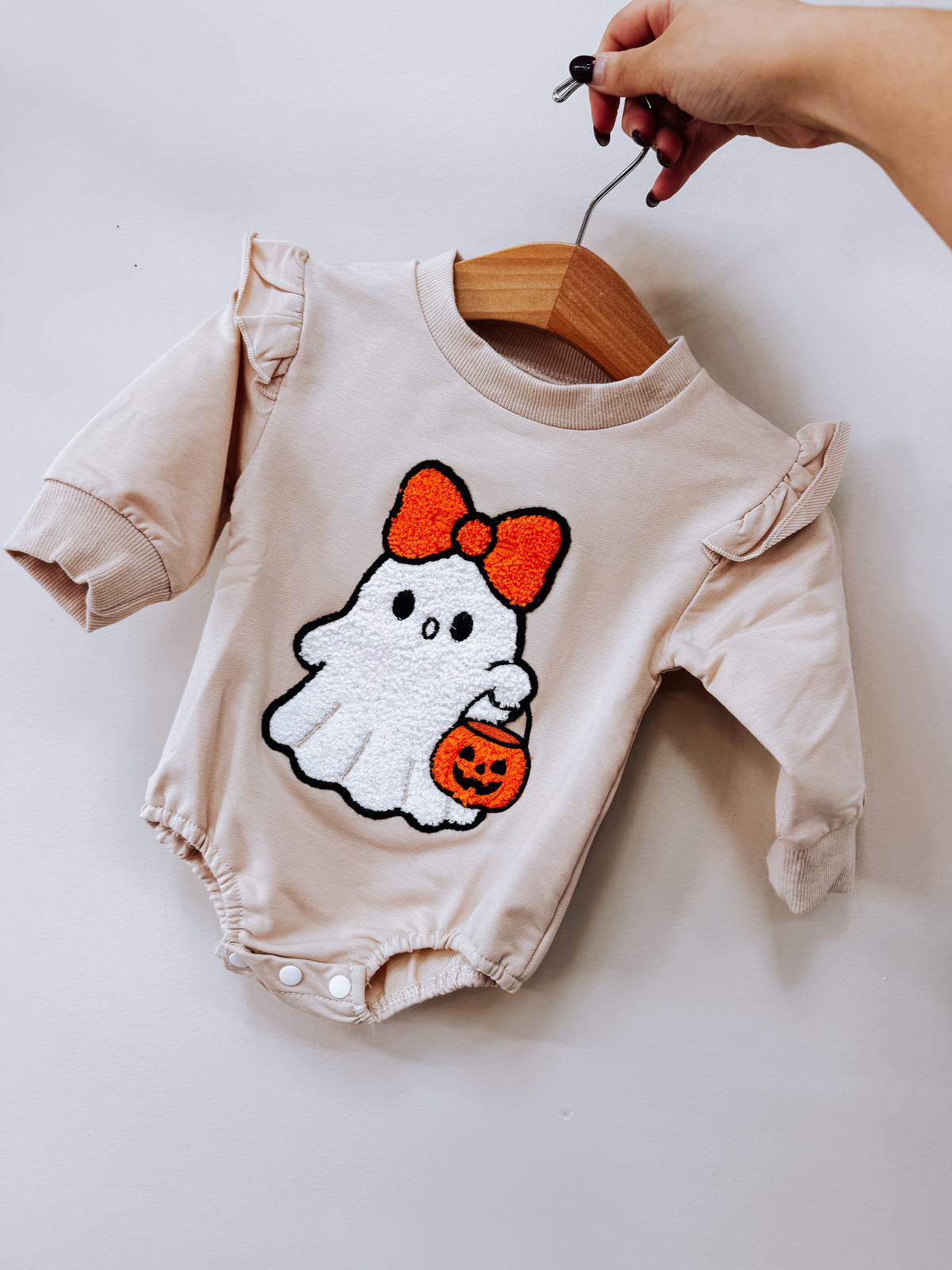 Light-colored long-sleeve Little Boo Ruffle Romper featuring a ghost applique with an orange bow and pumpkin treat bucket.