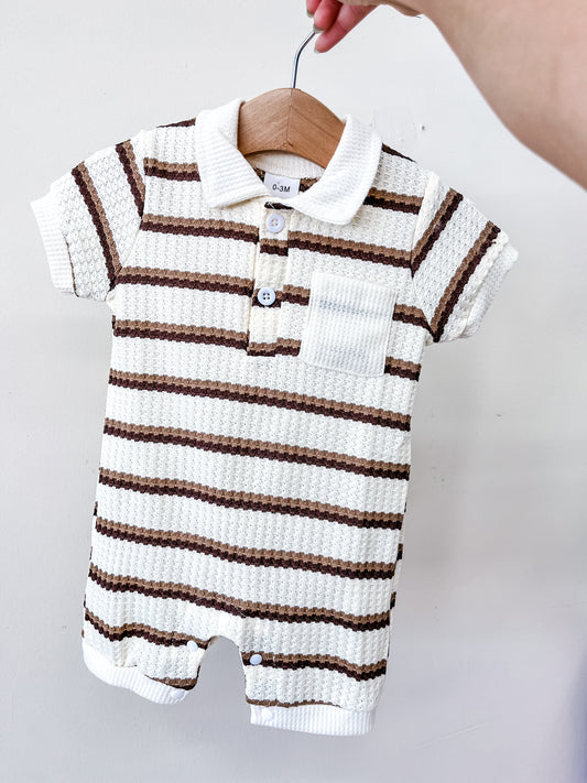 A hand holds a hanger with the Tiny Tot Bundles Cocoa Stripe Collard Romper—a short-sleeved, collared baby romper featuring white fabric with brown horizontal stripes, a front pocket, and buttons down the front.