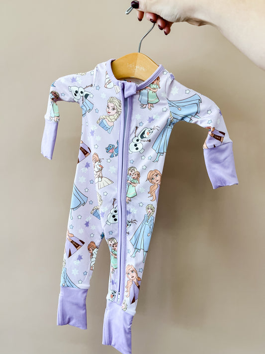 A hand holds a Snow Sisters Zippy by Tiny Tot Bundles. The purple onesie features Disney Frozen characters Elsa, Anna, and Olaf printed all over it.
