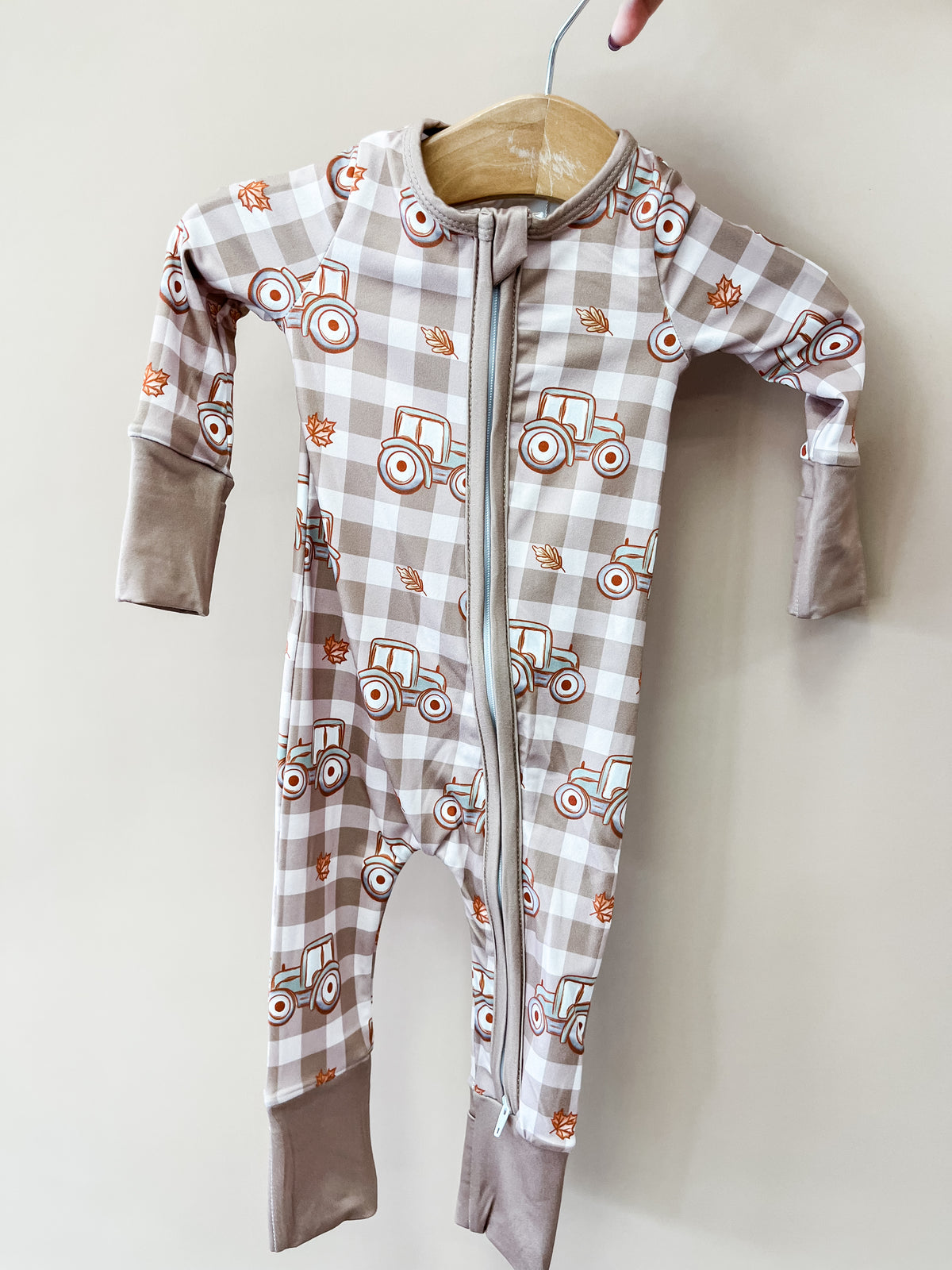 Tiny Tot Bundles Autumn Acres Zippy infant sleeper in a beige gingham pattern with orange tractors and autumn leaves, featuring a full-length front zipper.