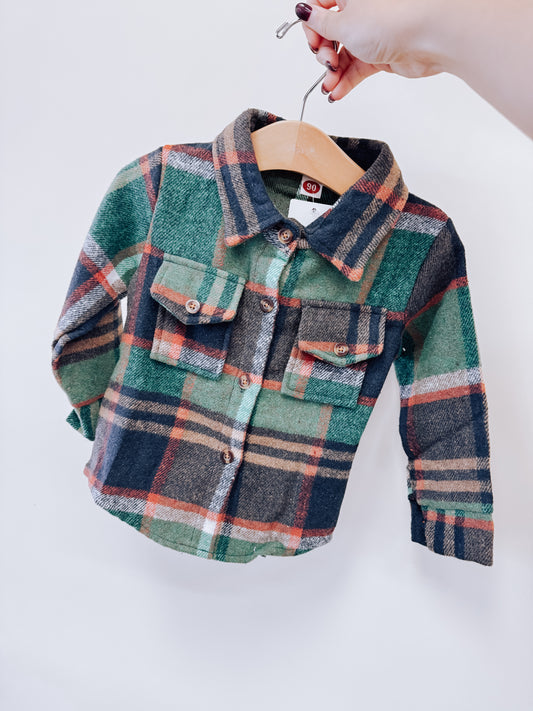 A hand holds a green, navy, and orange Evergreen Plaid Flannel shirt on a wooden hanger.