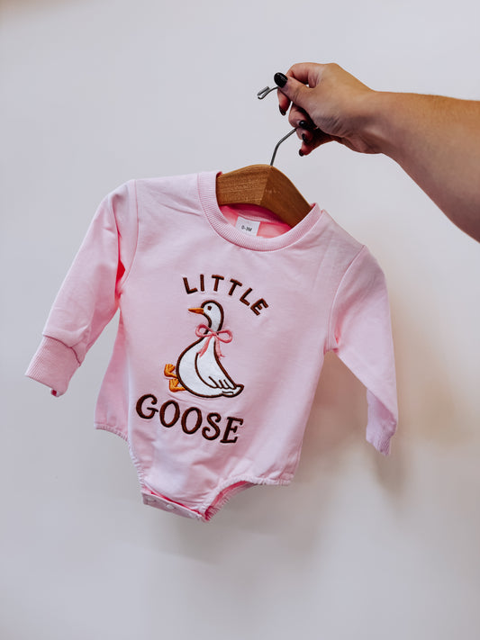 A hand holds a pink long-sleeved Tiny Tot Bundles Little Goose Embroidered Romper on a wooden hanger, featuring an embroidered goose and the text LITTLE GOOSE.