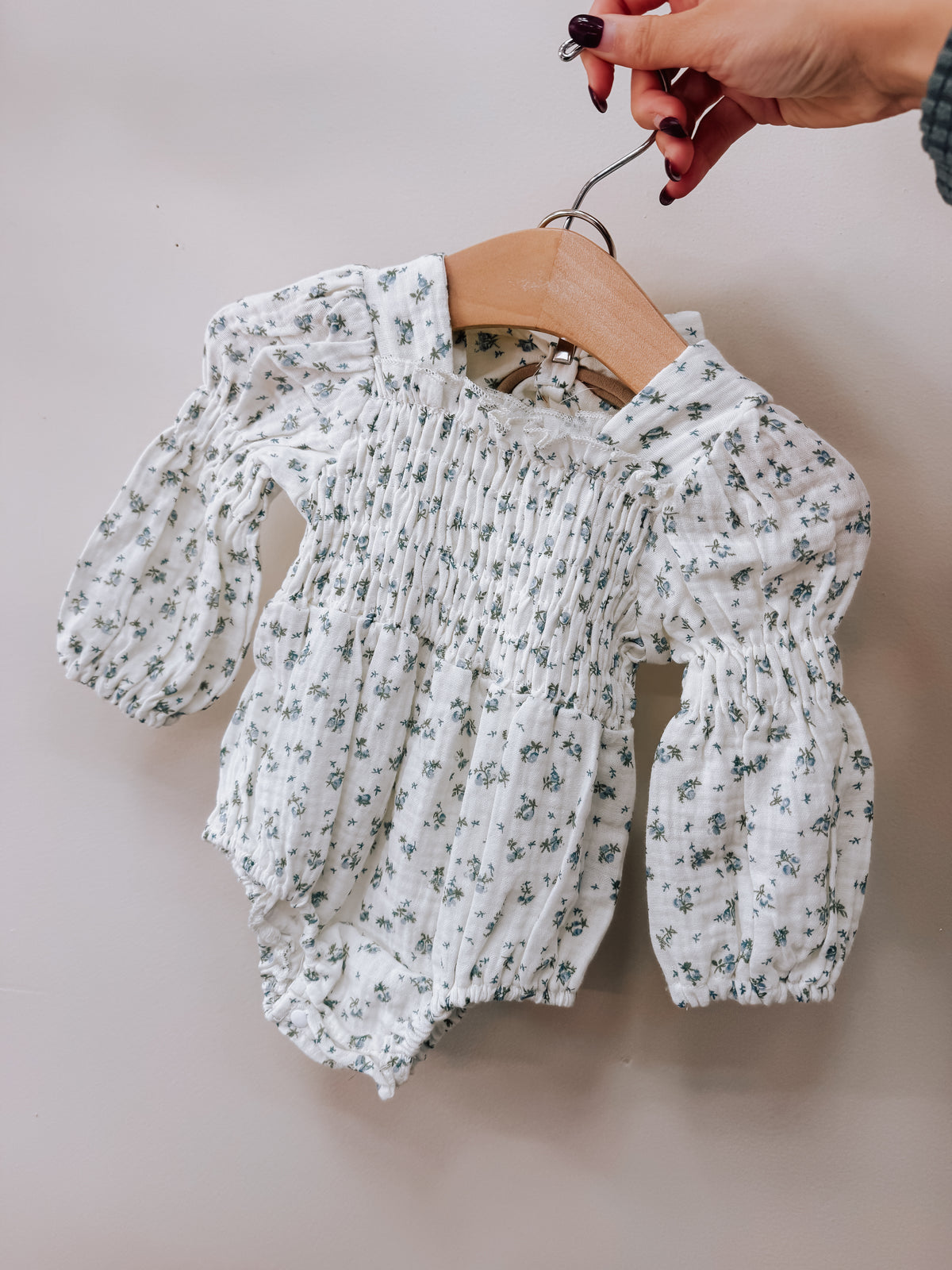 Tiny Tot Bundles Vintage Floral Smocked Romper, a long-sleeved baby romper with a smocked bodice and small blue floral print, hanging on a wooden hanger.