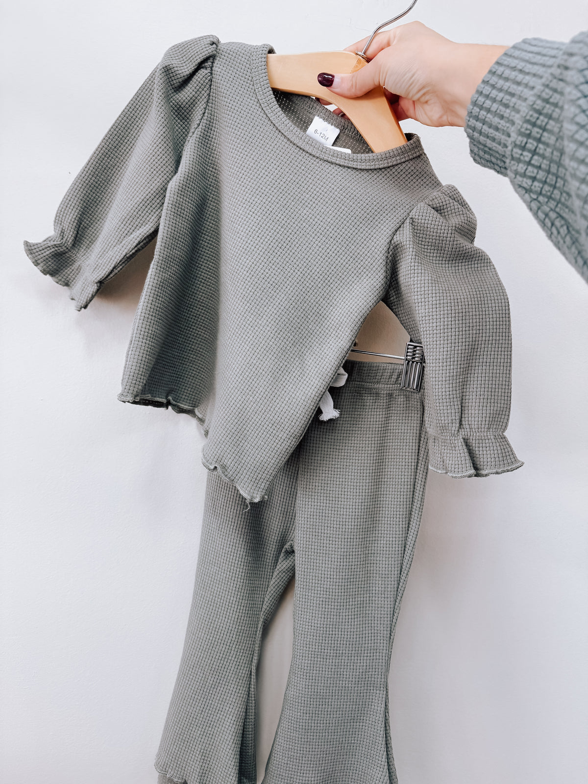 Sage Waffle Knit Ruffle Set in sage green with a long-sleeve top featuring ruffled cuffs and matching leggings on a wooden hanger.