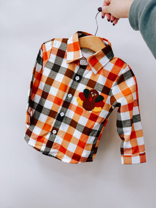 Tiny Tot Bundles Fall Plaid Turkey Shirt featuring a long-sleeved button-down design in an orange, white, and black plaid pattern with a small turkey patch on the chest.