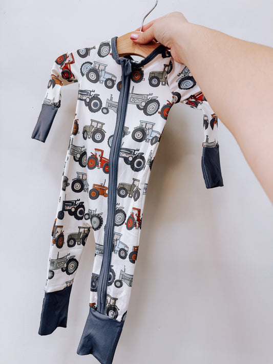 Tiny Tot Bundles Tractor Trails Zippy long-sleeved baby romper with a front zipper and dark gray cuffs, featuring an all-over print of colorful tractors.