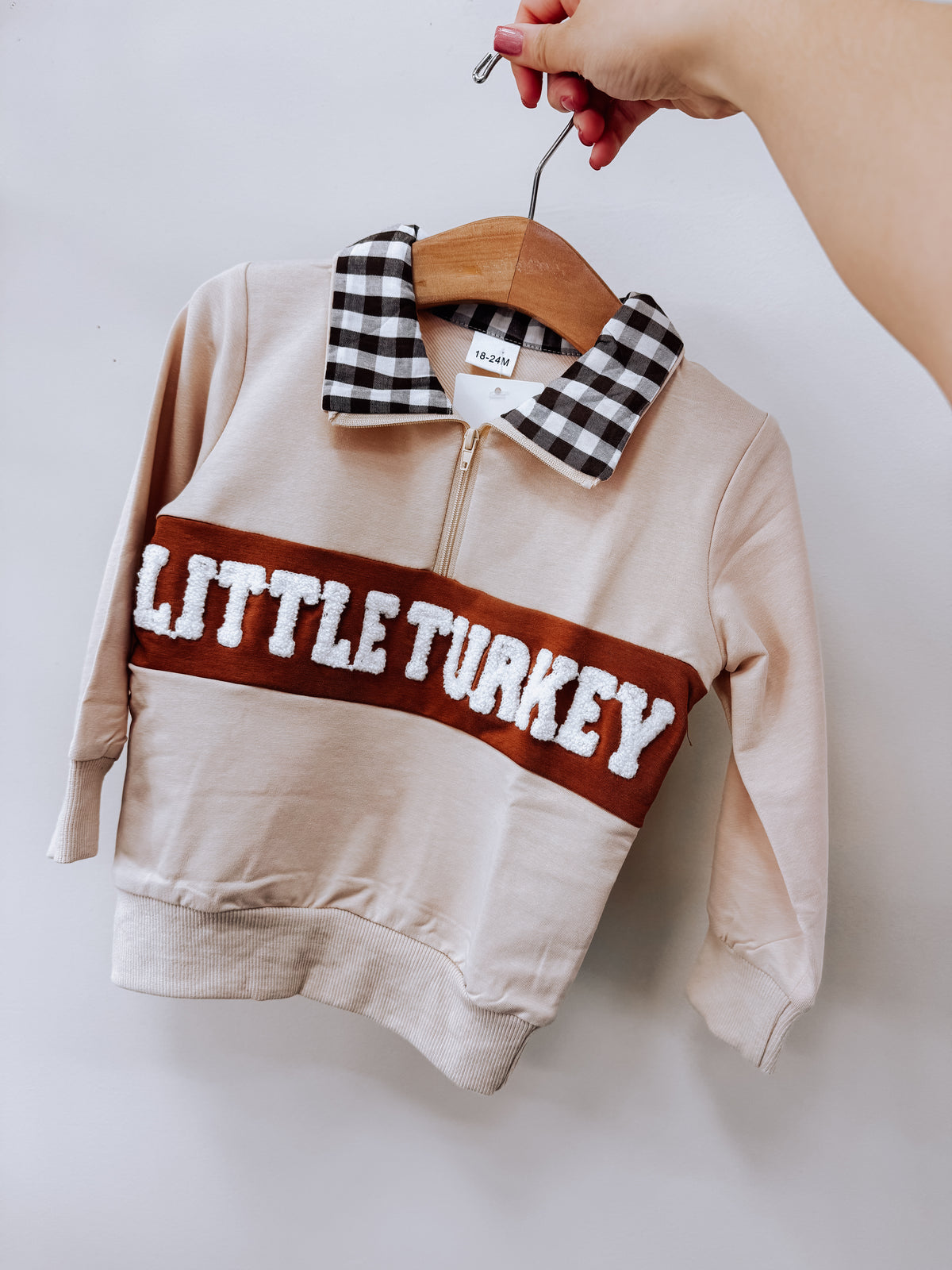 Tiny Tot Bundles Little Turkey Gingham Pullover, a tan long-sleeve pullover with a black-and-white gingham collar, a quarter-zip neckline, and the text LITTLE TURKEY in white textured letters on a brown horizontal chest stripe.