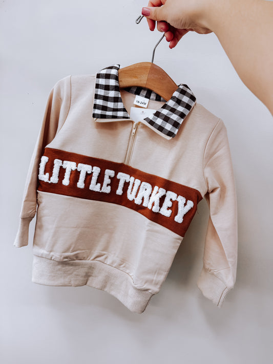 Tiny Tot Bundles Little Turkey Gingham Pullover, a tan long-sleeve pullover with a black-and-white gingham collar, a quarter-zip neckline, and the text LITTLE TURKEY in white textured letters on a brown horizontal chest stripe.