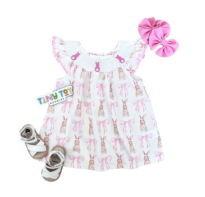 Flat lay of a Tiny Tot Bundles Bunny Smocked Dress, pink hair bow, white sandals, and a Tiny Tot Bundles card.