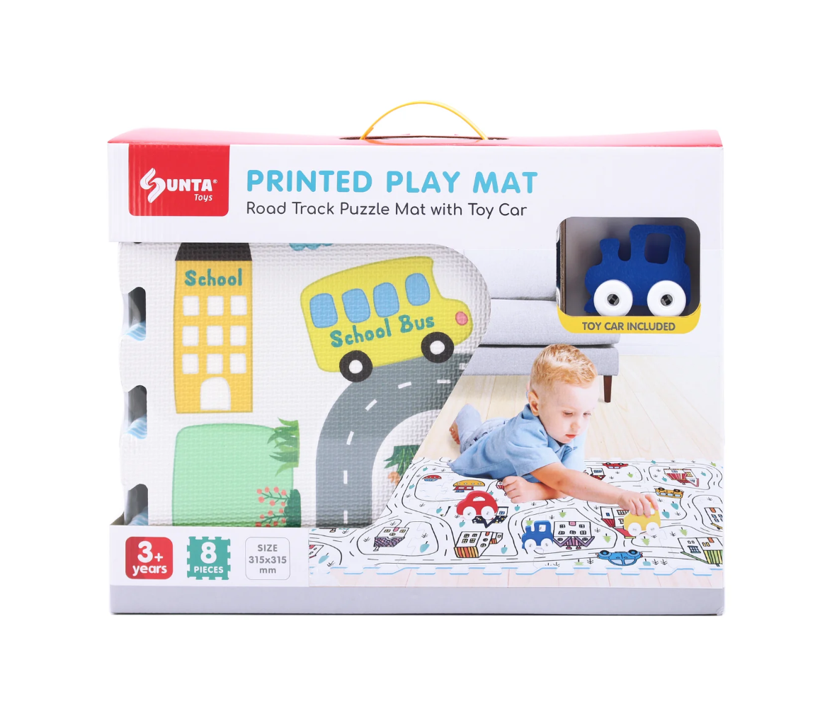 The Triaction Around The Town Play Mat is a 31.5" x 51" boxed set featuring a road track design, toy car and school bus, and is recommended for ages 3+. Shown with a young boy playing on the mat.