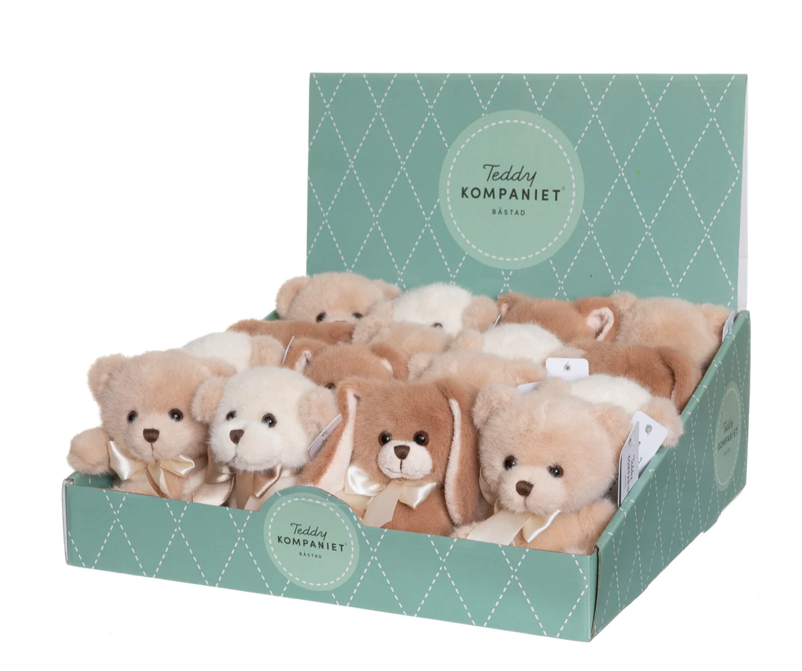 A green, diamond-patterned display box labeled "Triaction" holds soft Teddy Besties Companion plush bears in light brown, cream, and tan, each with a ribbon around its neck.