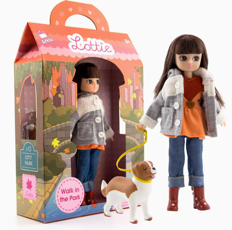 The Lottie Dolls - Walk In The Park by lootie dolls features a doll in a gray jacket, orange top, jeans, and brown boots holding a yellow leash with a white and brown dog, beside a colorful box with handle.