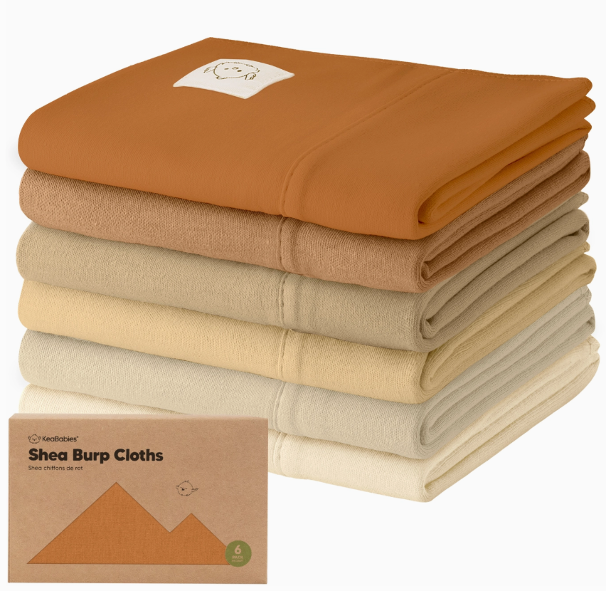A stack of six keababies 6-Pack Shea Burp Cloths in Terracotta shades, with a cartoon patch on the top cloth. In front is a boxed set labeled "Shea Burp Cloths.
