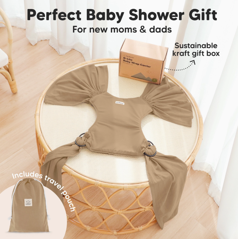 The keababies Baby Wrap Carrier - Warm Hearth (beige) is shown on a round wicker table with a matching travel pouch and sustainable kraft gift box. Text reads: Perfect Baby Shower Gift for new moms & dads. Includes travel pouch.