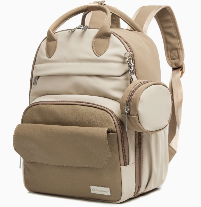 The keababies Diaper Bag Backpack in beige and light brown features multiple zippered compartments, a rounded front pocket, side pocket, padded shoulder straps, top handle, and a smooth, durable finish; includes a changing pad.