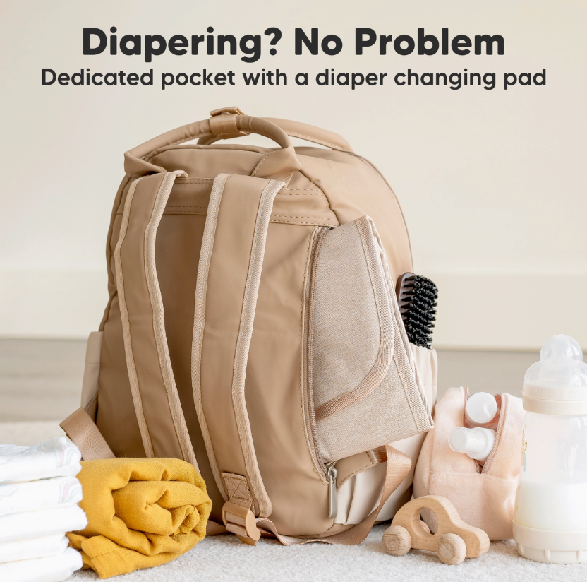 A keababies Diaper Bag Backpack, Baby Bag with Changing Pad is on the floor amid baby essentials—bottle, toy, brush, folded cloths, and plush item. Text above: "Diapering? No Problem.