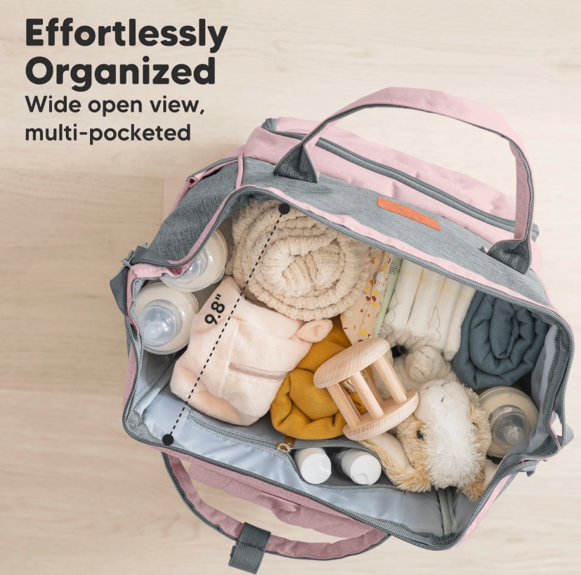 The keababies Diaper Bag Backpack - Pink Gray is open, displaying neatly arranged essentials like bottles, blankets, a plush toy, clothes, and a rattle. Text: Effortlessly Organized. Wide open view with multiple pockets.
