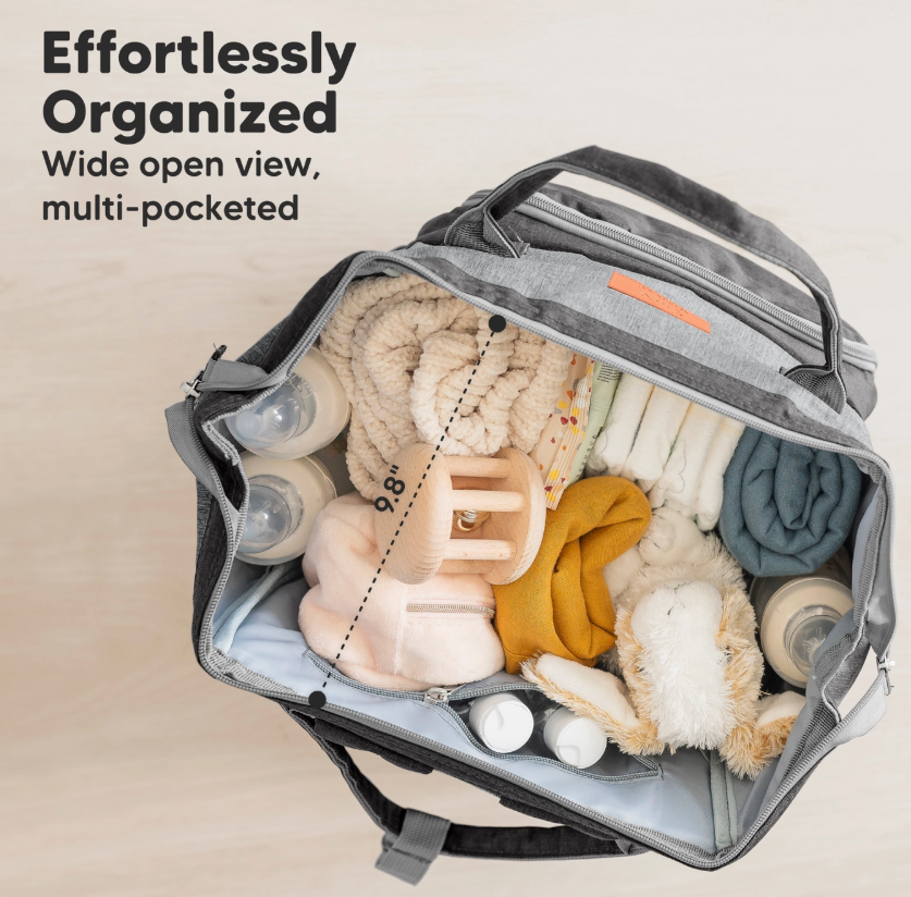The keababies Diaper Bag Backpack - Graphite is open, showing bottles, blankets, a stuffed animal, and toys organized in multiple pockets. Text: Effortlessly Organized. Wide open view, multi-pocketed.