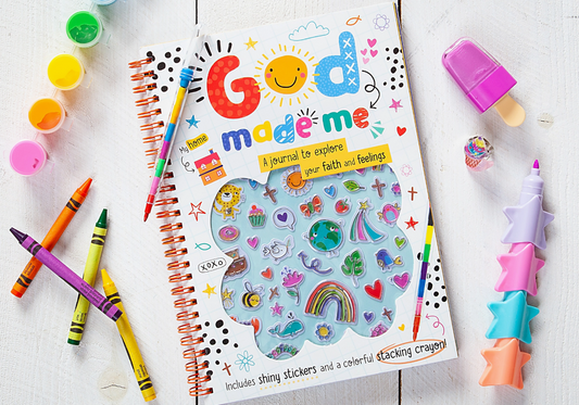 The God Made Me Kid's Journal Book by Broad Street Publishing Group features shiny stickers and a stacking star crayon, displayed on a white wooden table with crayons, paint pots, and a popsicle-shaped eraser.