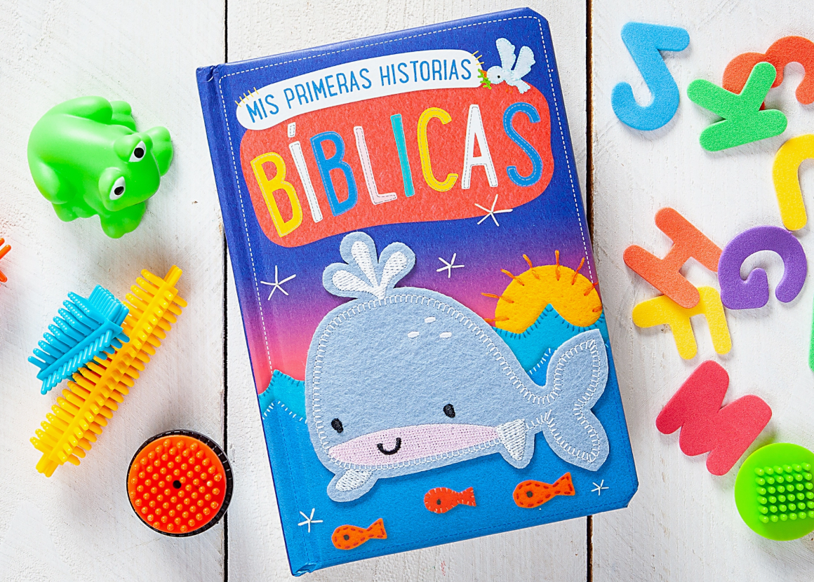 The Mis Primeras Historias Bíblicas Book by Broad Street Publishing Group features a felt whale on the cover, displayed with toys and foam numbers on a white wooden surface.