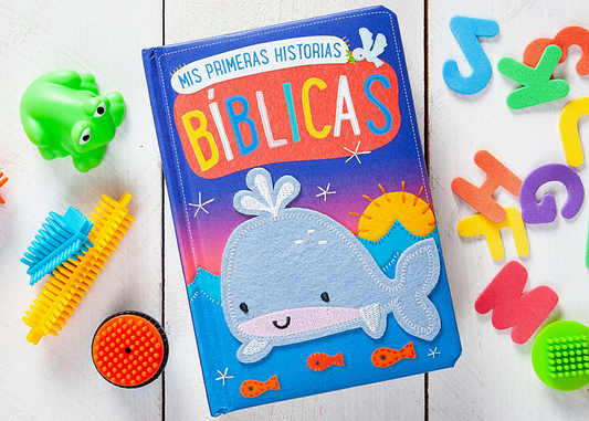 The Mis Primeras Historias Bíblicas Book by Broad Street Publishing Group features a felt whale on the cover, displayed with toys and foam numbers on a white wooden surface.