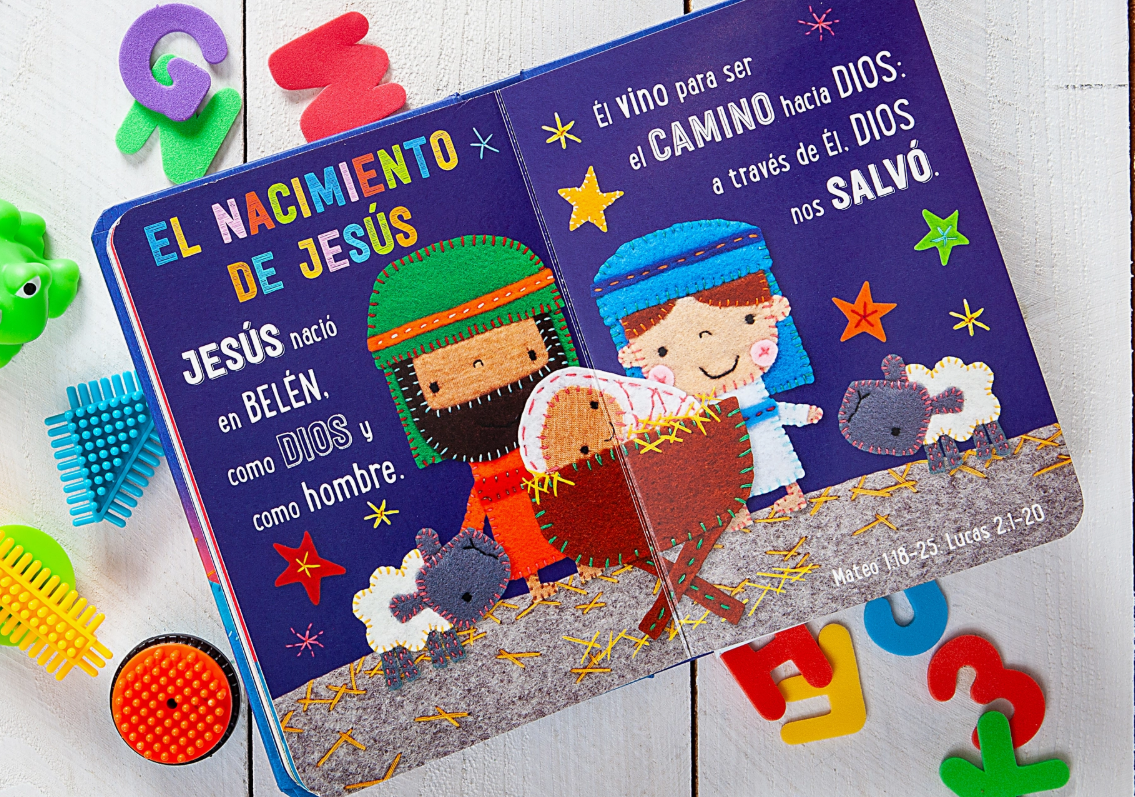 The Mis Primeras Historias Bíblicas book by Broad Street Publishing Group features a colorful nativity illustration with Mary, Joseph, baby Jesus, sheep, playful toys, and Spanish text about His birth and purpose.