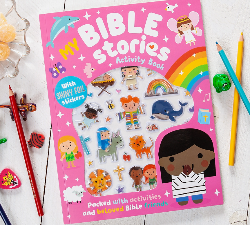 The My Bible Stories Activity Pink Book by Broad Street Publishing Group, featuring shiny foil stickers with animals and Bible characters, is placed on a white table with colored pencils, erasers, and a bowl of candy nearby.