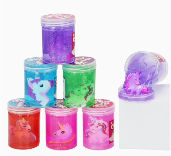 Six Capzone Unicorn Glitter Shimmer Gel Slime Mini Jars with unicorn art are stacked in a pyramid, with one purple jar tipped over to show a hidden purple unicorn toy inside. The scene is set against a white background.