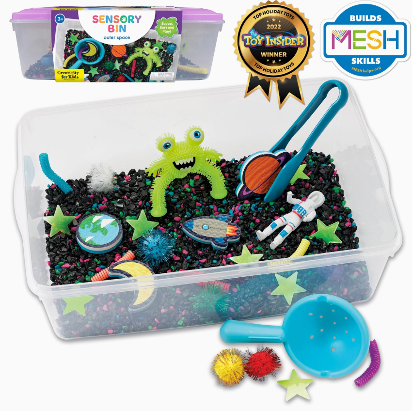 The Creativity For Kids Sensory Bin - Outer Space includes black rice, colorful space-themed toys (green monster, astronaut, planets, stars), blue scooping tools, and comes in packaging displaying award badges.